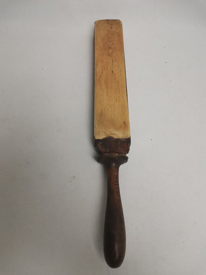 May include: A wooden strop with a light brown leather surface and a dark brown wooden handle.