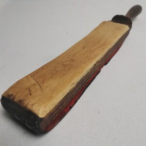 May include: A vintage wooden and leather strop for sharpening straight razors. The strop has a wooden handle and a leather strap with a red felt backing.