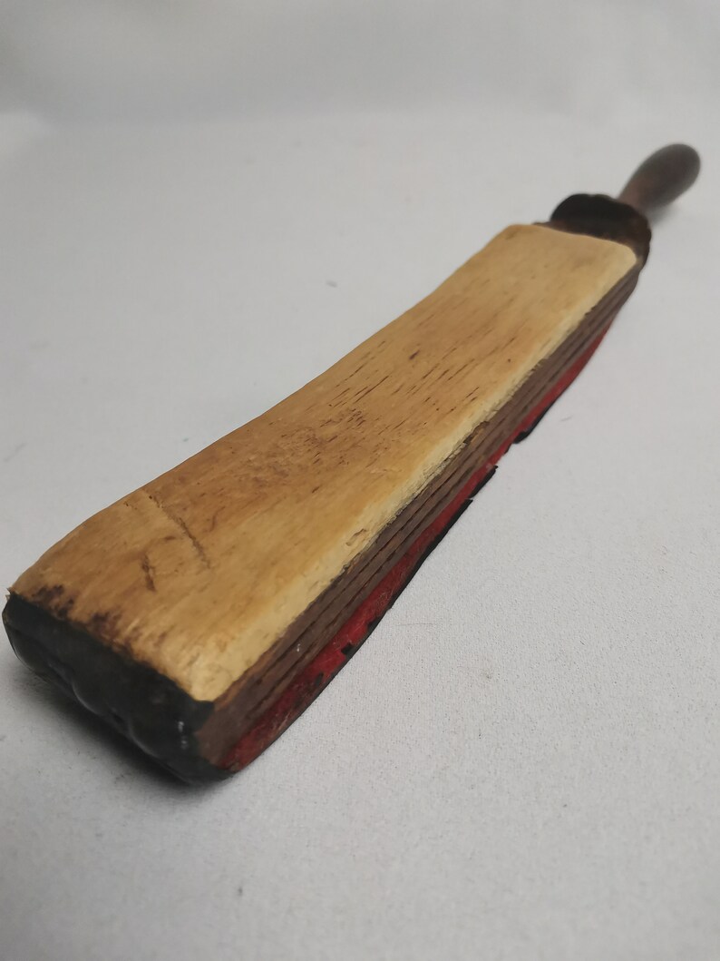 May include: A vintage wooden and leather strop for sharpening straight razors. The strop has a wooden handle and a leather strap with a red felt backing.