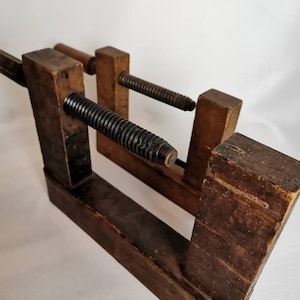 May include: Two antique wooden clamps with a threaded metal screw. The clamps are made of dark brown wood and have a rustic appearance.