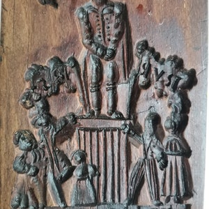 May include: A wooden cookie mould with a raised design of a man in a hat standing on a platform with people surrounding him. The text "REMEMBRANCE" is carved into the bottom of the mould.