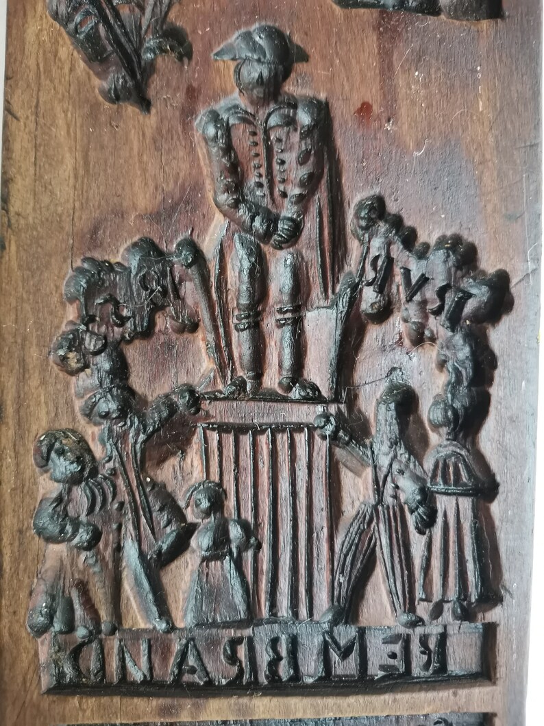 May include: A wooden cookie mould with a raised design of a man in a hat standing on a platform with people surrounding him. The text "REMEMBRANCE" is carved into the bottom of the mould.