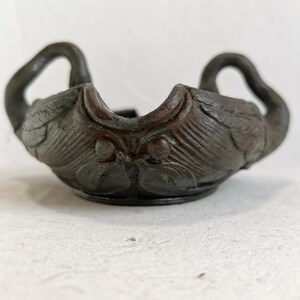 May include: A dark brown, antique-style bowl with swan-shaped handles. The bowl features detailed carvings of feathers and swan heads, creating a vintage aesthetic. The bowl is likely made of a durable material, suitable for decorative or functional use.