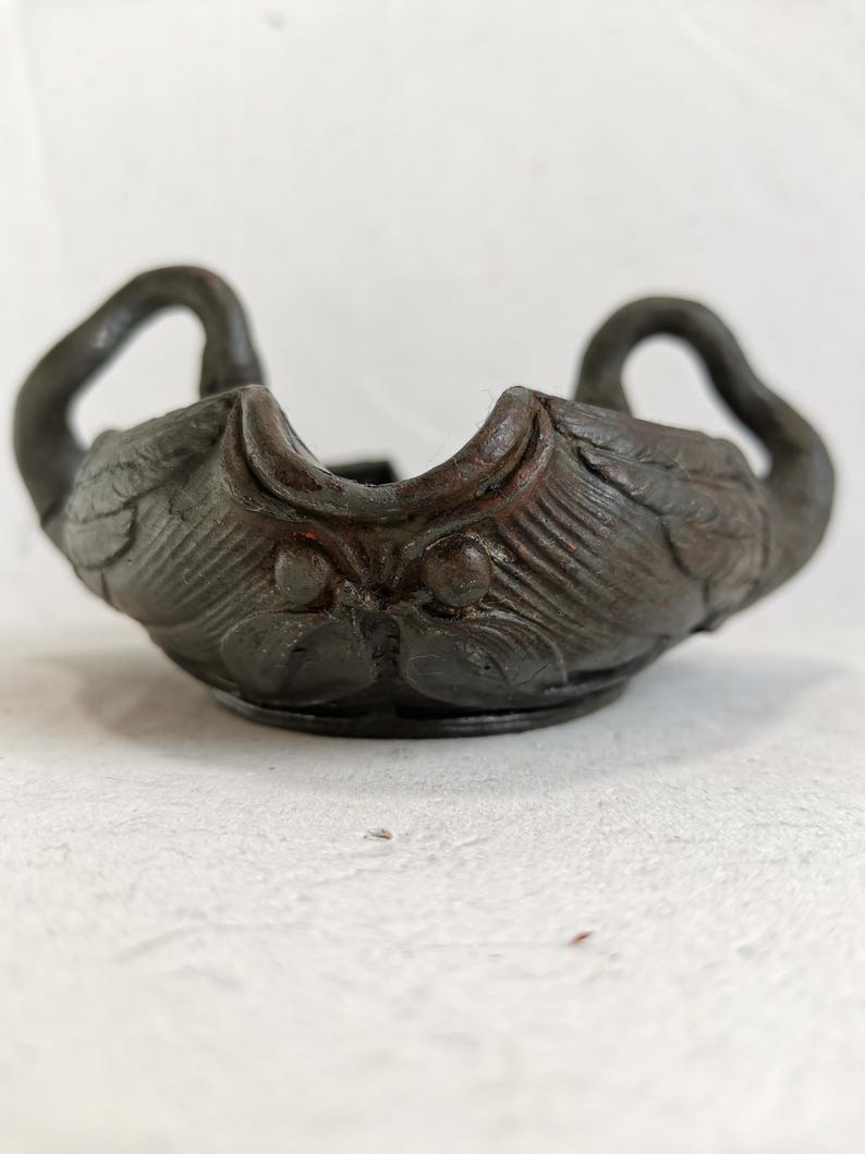 May include: A dark brown, antique-style bowl with swan-shaped handles. The bowl features detailed carvings of feathers and swan heads, creating a vintage aesthetic. The bowl is likely made of a durable material, suitable for decorative or functional use.