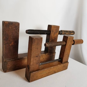 May include: Two vintage wooden clamps with metal screws and handles. The clamps are made of dark brown wood and have a rustic appearance.