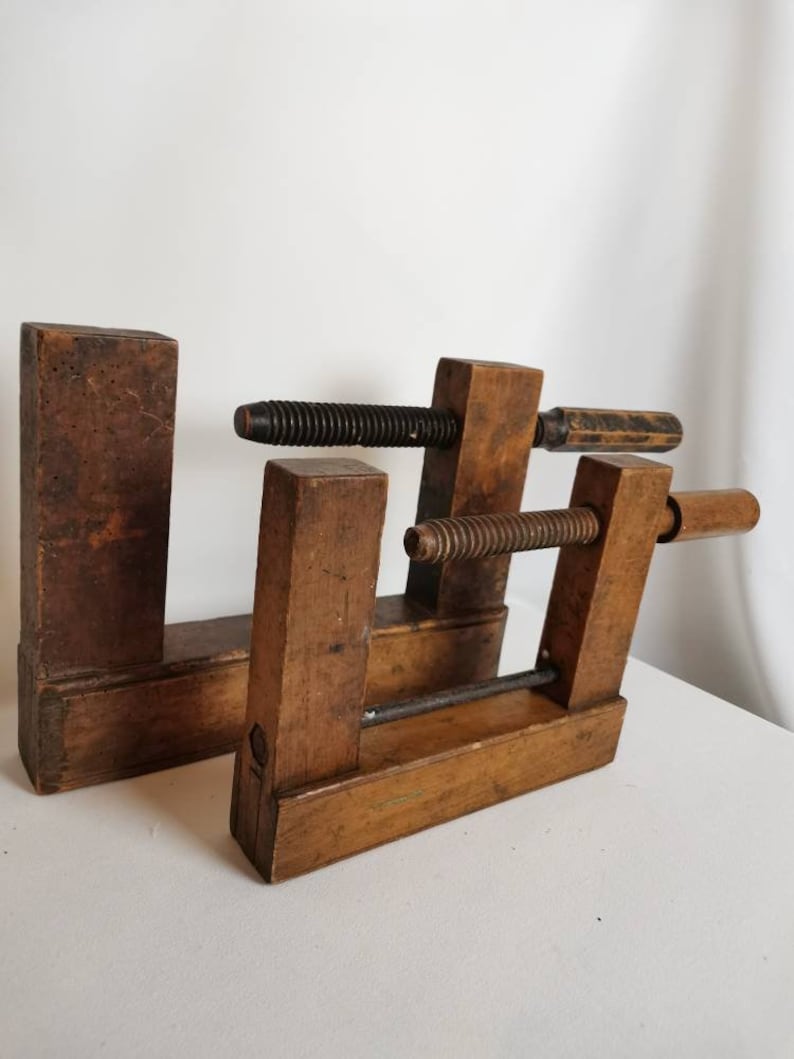 May include: Two vintage wooden clamps with metal screws and handles. The clamps are made of dark brown wood and have a rustic appearance.