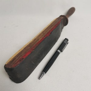 May include: A vintage leather strop with a wooden handle. The strop is made of layered wood and has a red stripe. The strop is about 12 inches long and 2 inches wide.