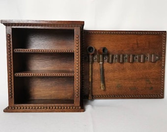 May include: A wooden pipe rack with a shelf for storing pipes. The rack has a decorative beaded trim and is made of dark wood. The rack is open and has a shelf on the left side and a pipe rack on the right side.