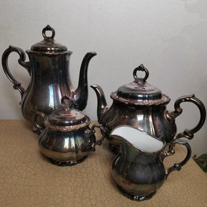 Puede incluir: Un juego de té de plata con tetera, jarra de crema, azucarero y cafetera. El juego tiene un acabado brillante e iridiscente.