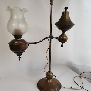 May include: A vintage brass and copper table lamp with two shades. The lamp has a white frosted glass shade and a brass shade. The lamp has a long, curved arm and a round base.