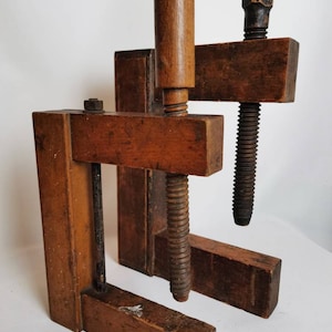 May include: Two antique wooden clamps with metal screws and wooden handles. The clamps are made of dark brown wood and have a rustic appearance.