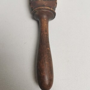 May include: A wooden strop with a dark brown leather surface and a wooden handle. The leather surface has a row of small metal rivets.