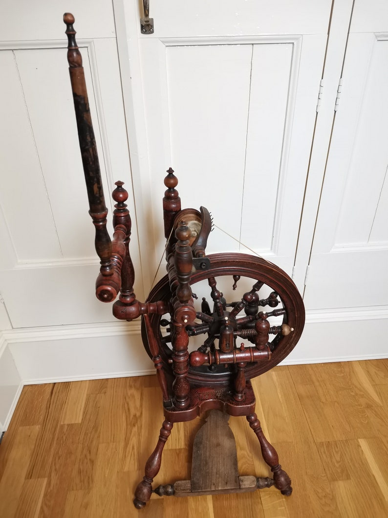 May include: A wooden spinning wheel with a large wheel and a spindle. The wheel is made of dark wood and has a decorative design. The spindle is made of light wood and has a small knob on the end.