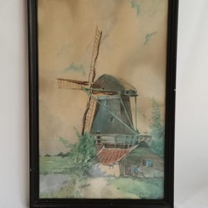 May include: A watercolor painting of a windmill in a rural landscape. The windmill is painted in shades of brown and green, with a red roof. The sky is a soft blue with white clouds. The painting is framed in a black frame.