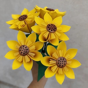 A bouquet of five yellow origami sunflowers with green paper leaves and a brown button in the centre of each flower