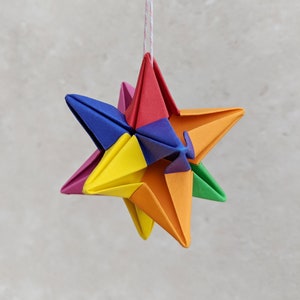 Origami 3d paper star hanging from a loop of twine. The star is folded from six colours of paper to create a rainbow effect