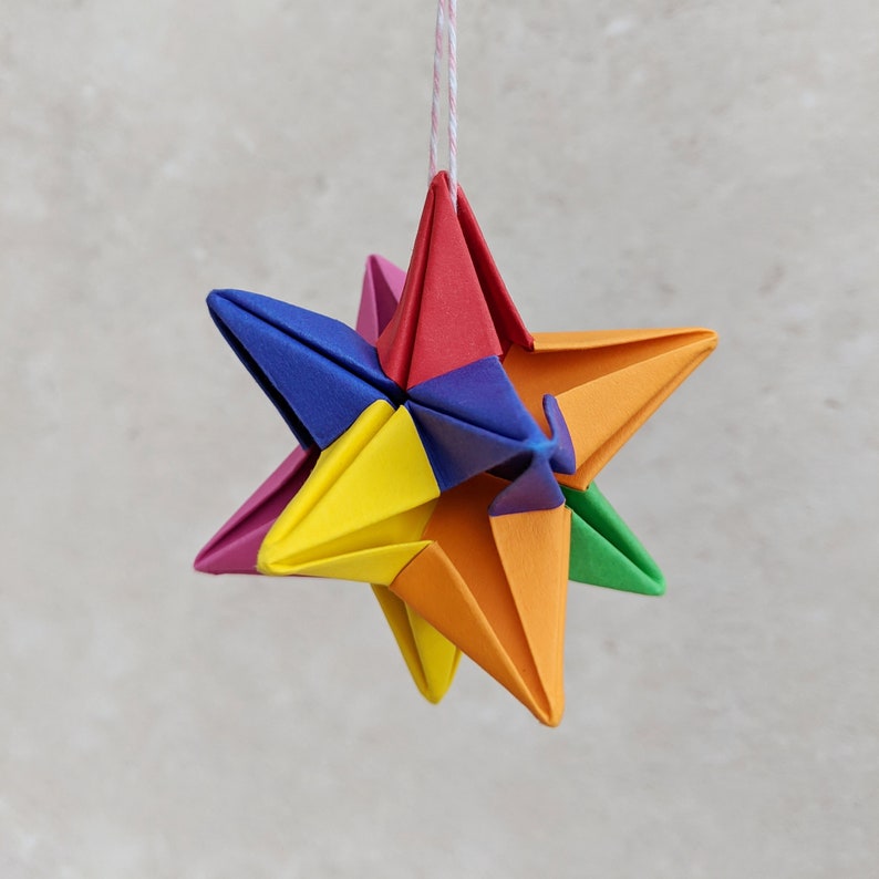 Origami 3d paper star hanging from a loop of twine. The star is folded from six colours of paper to create a rainbow effect