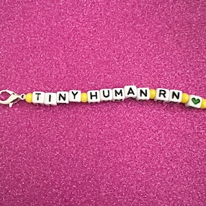 May include: White and yellow beaded keychain with the words "TINY HUMAN RN" and a green heart charm.