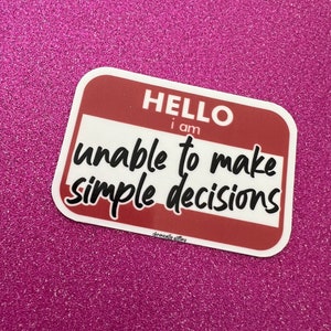 May include: A white sticker with a red border and the text "HELLO I am unable to make simple decisions" on a pink glitter background.