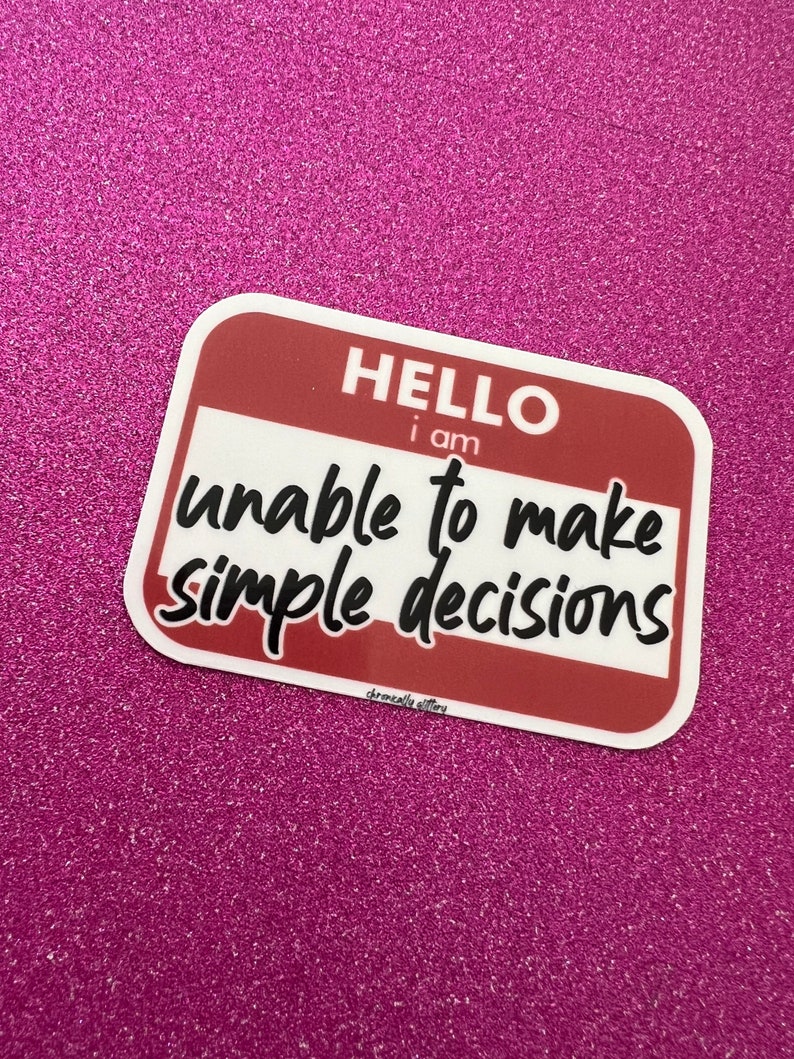 May include: A white sticker with a red border and the text "HELLO I am unable to make simple decisions" on a pink glitter background.