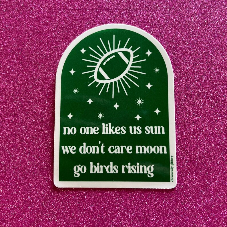 May include: Green and white sticker with a football shaped sun and stars. The text reads "no one likes us sun we don't care moon go birds rising".
