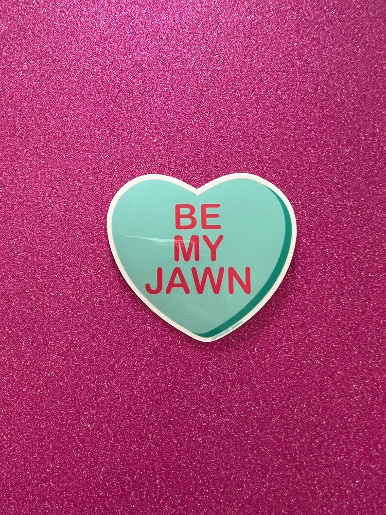 May include: A light blue heart-shaped sticker with the text "BE MY JAWN" in red letters. The sticker is on a pink glitter background.