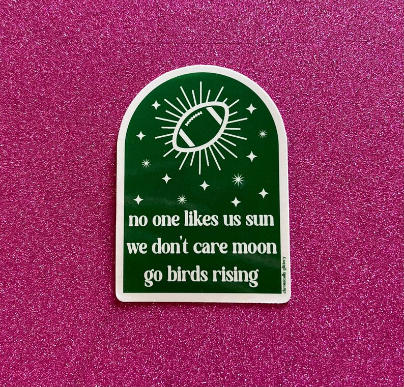 May include: Green and white sticker with a football and stars. The text reads "no one likes us sun we don't care moon go birds rising".