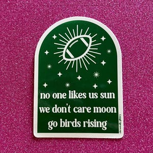 May include: Green sticker with a white football inside a sunburst design. The text reads "no one likes us sun we don't care moon go birds rising".