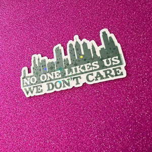 May include: A white sticker with a black and gray cityscape silhouette and the text "NO ONE LIKES US WE DON'T CARE" in black.