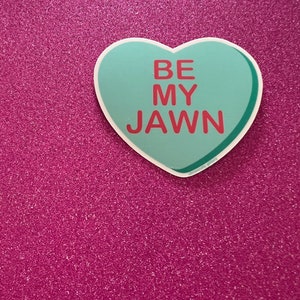 May include: A teal heart-shaped sticker with the text "BE MY JAWN" in red letters on a pink glitter background.