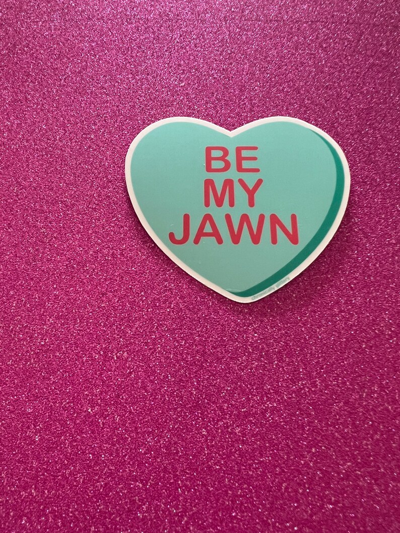 May include: A teal heart-shaped sticker with the text "BE MY JAWN" in red letters on a pink glitter background.