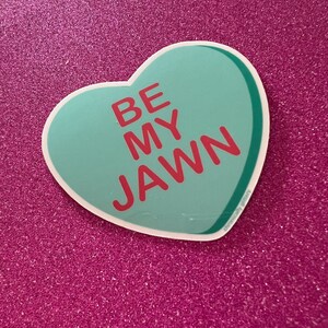 May include: A teal heart-shaped sticker with the text "BE MY JAWN" in red letters.