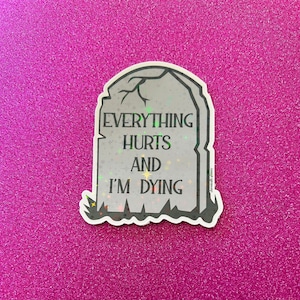 May include: A white sticker with a gray tombstone design. The tombstone has the text "Everything Hurts And I'm Dying" on it.