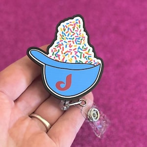 May include: A blue badge reel featuring a bowl of colorful sprinkles with a red "J" on the bowl. The badge reel has a black outline and a clear plastic retractable cord.