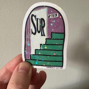 May include: A sticker with a glittery finish featuring a green staircase leading to a purple door with the word "SUR" on it. The door has a white number "8759" above it. The sticker has the text "CHRONICALLY GLITTERY" at the bottom.