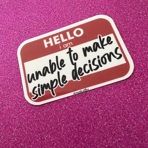 May include: A white sticker with a red border and rounded corners. The sticker says "HELLO I AM unable to make simple decisions" in black text.