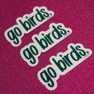 May include: Three white stickers with the text "go birds." in dark green lettering on a pink sparkly background.