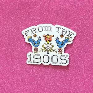 May include: A white sticker with a cross-stitch design featuring two blue birds, a red flower, and the text "From the 1900s".