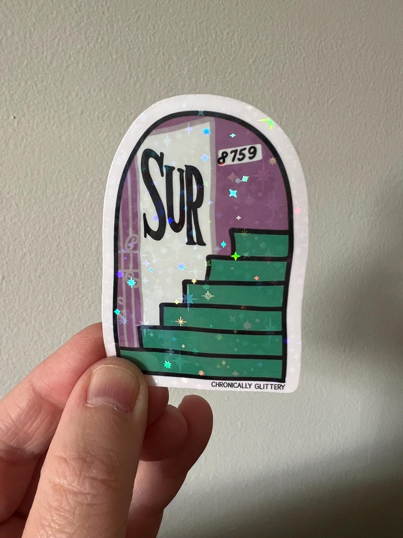 May include: A holographic sticker featuring a purple door with the word "SUR" on it and a green staircase leading up to the door. The door has the number "8759" on it. The sticker has a glittery finish and the text "CHRONICALLY GLITTERY" at the bottom.