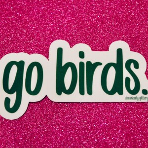 May include: Green "go birds" sticker on a pink glitter background.