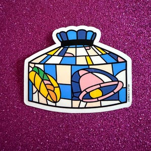 May include: A die-cut sticker featuring a stained glass lamp design with a blue, white, and yellow grid pattern. The lamp shade displays a yellow taco and a pink bell graphic. The text Chronically Glittery is printed vertically on the right side.