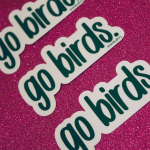 May include: Three white stickers with the text "go birds" written in dark green. The stickers are on a pink sparkly background.