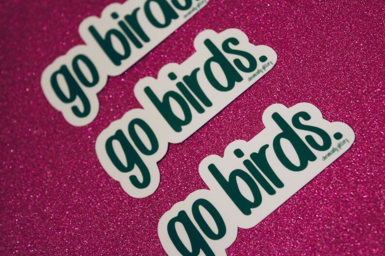 May include: Three white stickers with the text "go birds" written in dark green. The stickers are on a pink sparkly background.