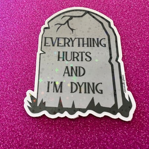 May include: A gray tombstone sticker with a glittery finish. The sticker reads "Everything Hurts And I'm Dying".