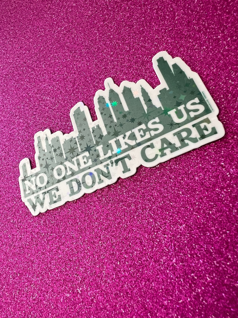 May include: A white sticker with a black cityscape silhouette and the text "No one likes us we don't care". The sticker has a holographic finish.