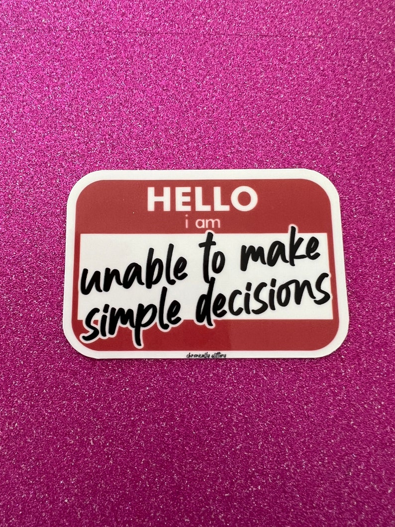 May include: A red and white name tag sticker with the text "HELLO i am unable to make simple decisions" in black cursive font.