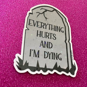 May include: A gray tombstone sticker with the text "Everything Hurts And I'm Dying" in black lettering. The sticker has a glittery finish and a black outline.