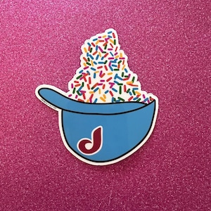 May include: A blue and white sticker of a bowl filled with colorful sprinkles. The bowl has a red "J" logo.