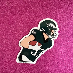 May include: A green and black sticker of an American football player wearing a helmet and jersey with the Philadelphia Eagles logo. The player is holding a football and running. The sticker has the text "Chronically Glittery" at the bottom.
