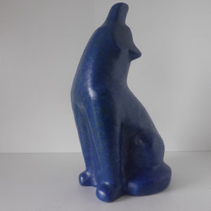 Könnte beinhalten: Eine blaue Keramikskulptur eines Wolfes, der zum Mond heult. Die Skulptur sitzt mit dem Kopf nach hinten geneigt und dem Maul offen.